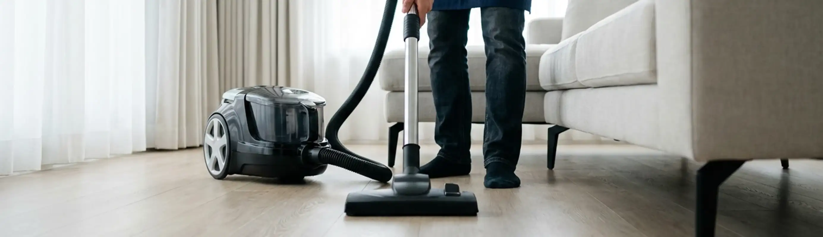 Professional house cleaner vacuuming a living room floor with a canister vacuum cleaner, Tempe, AZ.