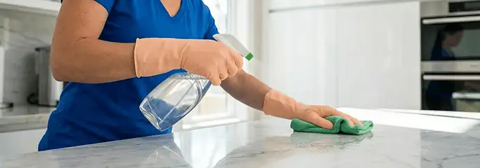 Maid service worker spraying and wiping a kitchen countertop with a microfiber cloth for sanitizing, Tempe, AZ.