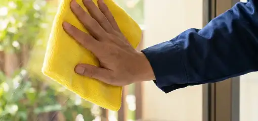 House cleaner wiping a glass window with a yellow microfiber cloth for streak-free cleaning, Tempe, AZ.